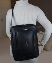 Woman in a grey jumper wearing the AVAIA bag in Noir as a crossbody bag in vertical position.