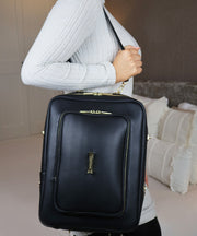 Woman wearing a crossbody AVAIA bag by brand LIAVELLA in a bedroom setting.