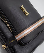 Load image into Gallery viewer, AVAIA bag in Noir, showing the fabric striped strap, with a focus on the gold hardware and the visible brand name LIAVELLA, all against a light gray background.
