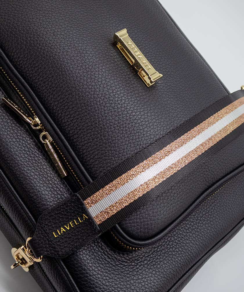 AVAIA bag in Noir, showing the fabric striped strap, with a focus on the gold hardware and the visible brand name LIAVELLA, all against a light gray background.