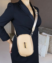 AVAIA Petit in creme caramel in the crossbody configuration and the fabric strap.  Person is wearing a black jacket and is indoors.