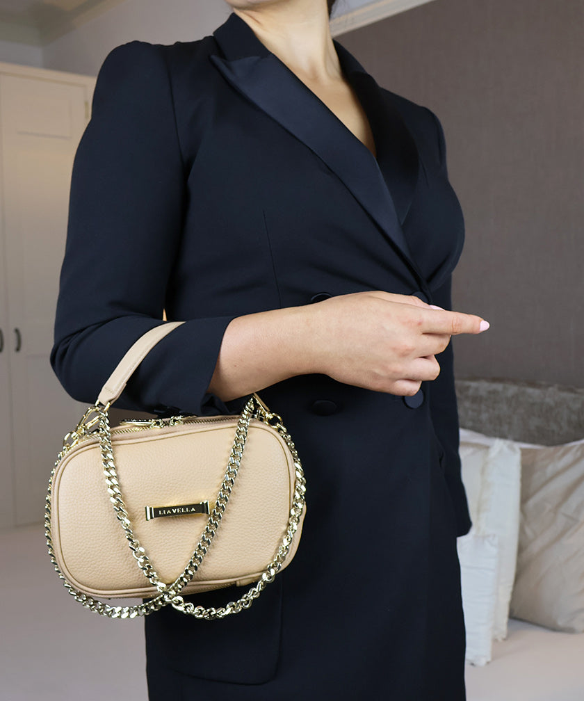 Person holding the AVAIA Petit handbag over the arm with a chain detail strap, wearing a dark blazer indoors.
