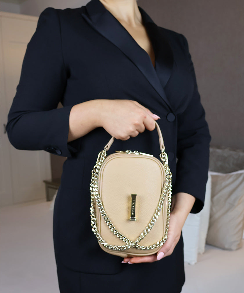 Person in an indoor room, holding the AVAIA Petit in creme caramel with a gold chain strap.