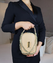 Person in an indoor room, holding the AVAIA Petit in creme caramel with a gold chain strap.