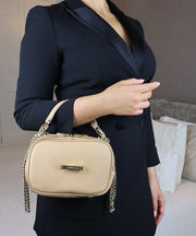 Person holding the AVAIA Petit in horizontal configuration with a gold chain strap in an indoor setting.