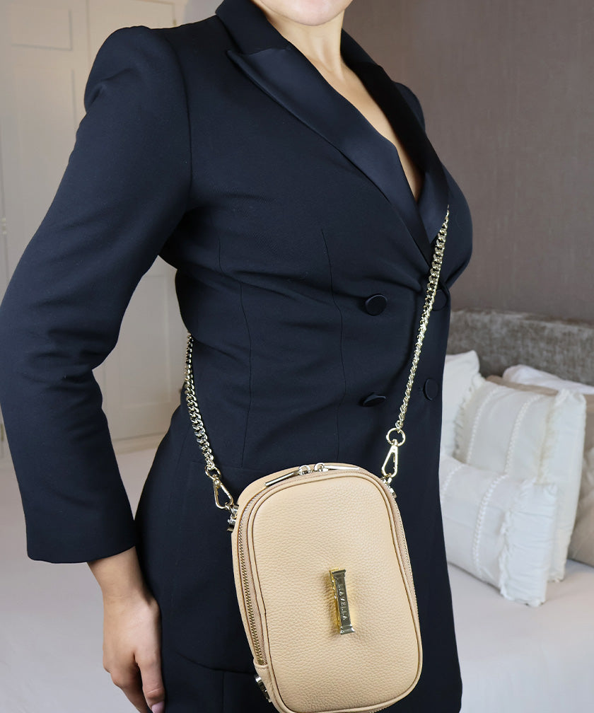 Person wearing a navy blazer with the AVAIA Petit as crossbody bag in vertical configuration in an indoor setting.