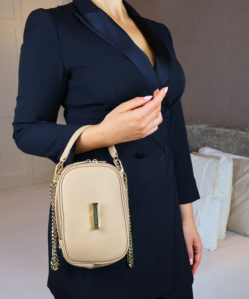 Woman in a room holding the AVAIA Petit bag over her arm showing a luxurious gold chain strap.