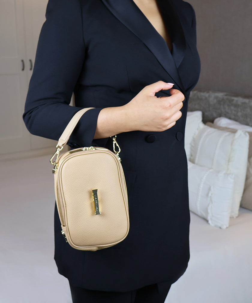 Woman in a dark blazer wearing the AVAIA Petit as a wristlet bag, in an indoor setting.