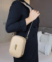 Person wearing the AVAIA Petit in Creme Caramel as a crossbody bag with a visible brand logo, standing indoors.
