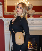 Load image into Gallery viewer, Woman wearing the AVAIA Petit as a crossbody bag in a room with a fireplace and decorative mirror.
