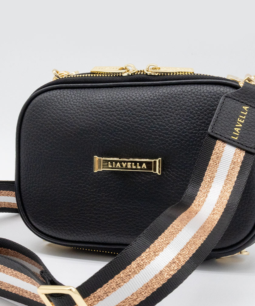 AVAIA Petit in Noir with gold pillar of strength clip and a striped strap on a light gray background.
