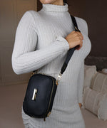 Load image into Gallery viewer, A woman in a grey sweater wearing an AVAIA Petit as a crossbody bag in an indoor setting.
