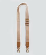Load image into Gallery viewer, A wide fabric strap in creme caramel, with leather accents and gold hardware, against a white background.
