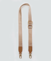 A wide fabric strap in creme caramel, with leather accents and gold hardware, against a white background.