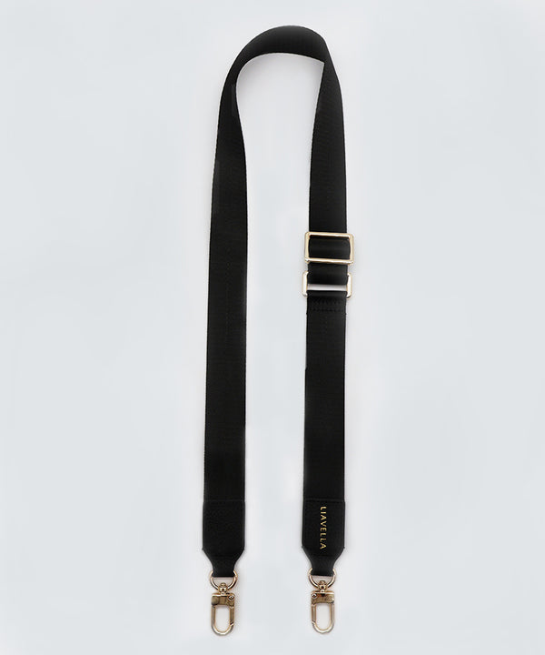 Adjustable, black fabric bag strap with gold hardware on a white background.
