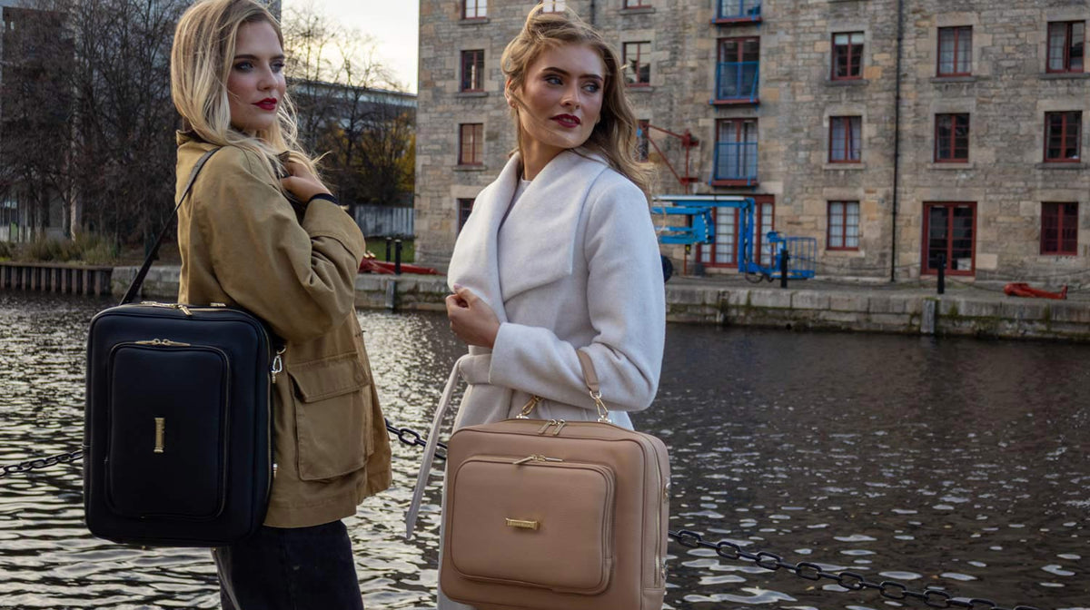 Two women holding the AVAIA bag in different configurations, standing by a canal in Edinburgh with buildings in the background.
