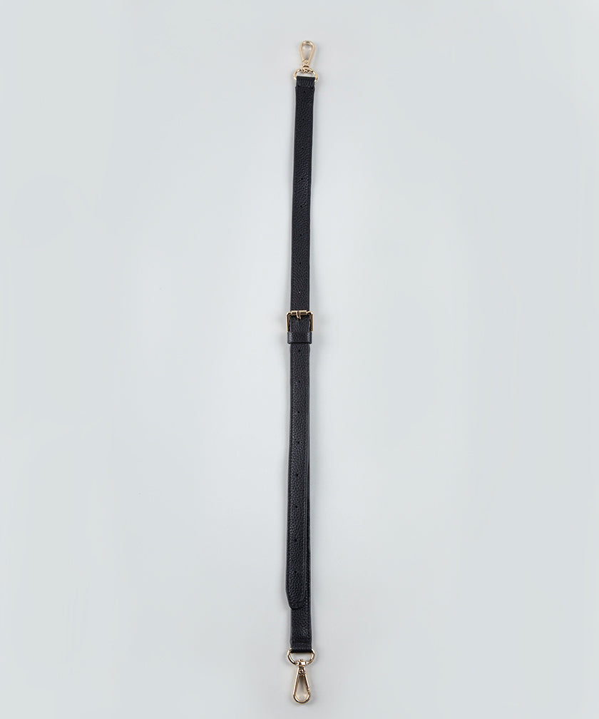 Black bag strap with gold hardware on a light gray background