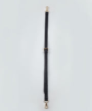 Black bag strap with gold hardware on a light gray background