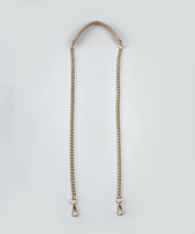 Gold chain strap with a leather handle against  a light gray background.