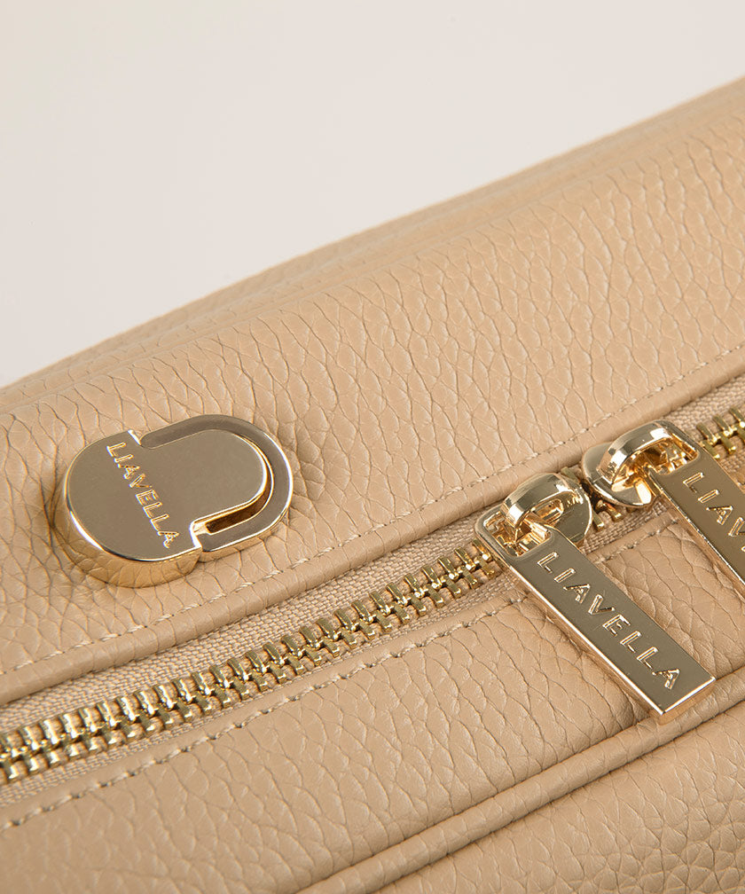 Close-up of the AVAIA bag pebbled leather and the branded "LIVAELLA" gold hardware including the zip and multi-anchor point, on a light gray background.