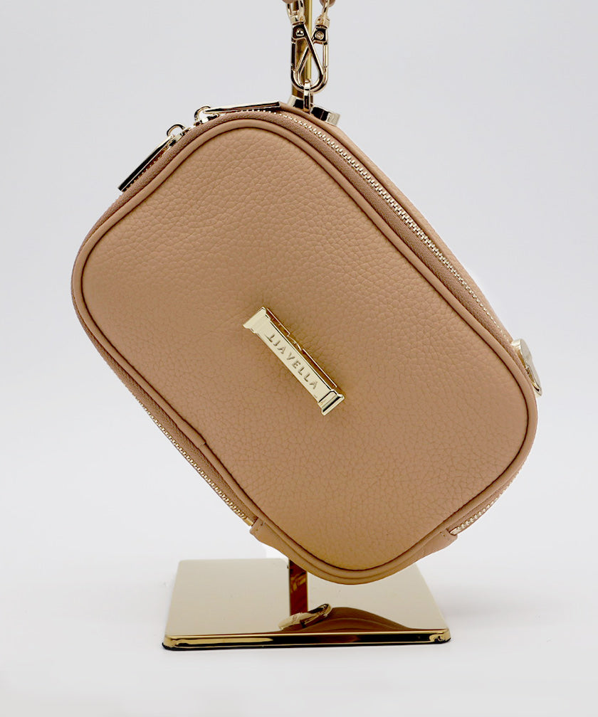 The AVAIA Petit in Creme Caramel with gold hardware, hanging on a gold stand, against a white background.