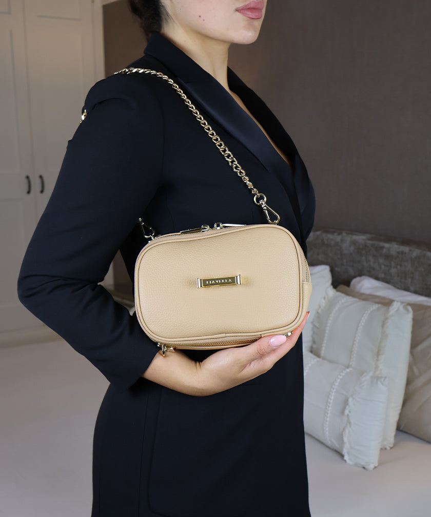 Person in a room holding the avaia petit in creme caramel in horizontal orientation, showcasing the chain strap.