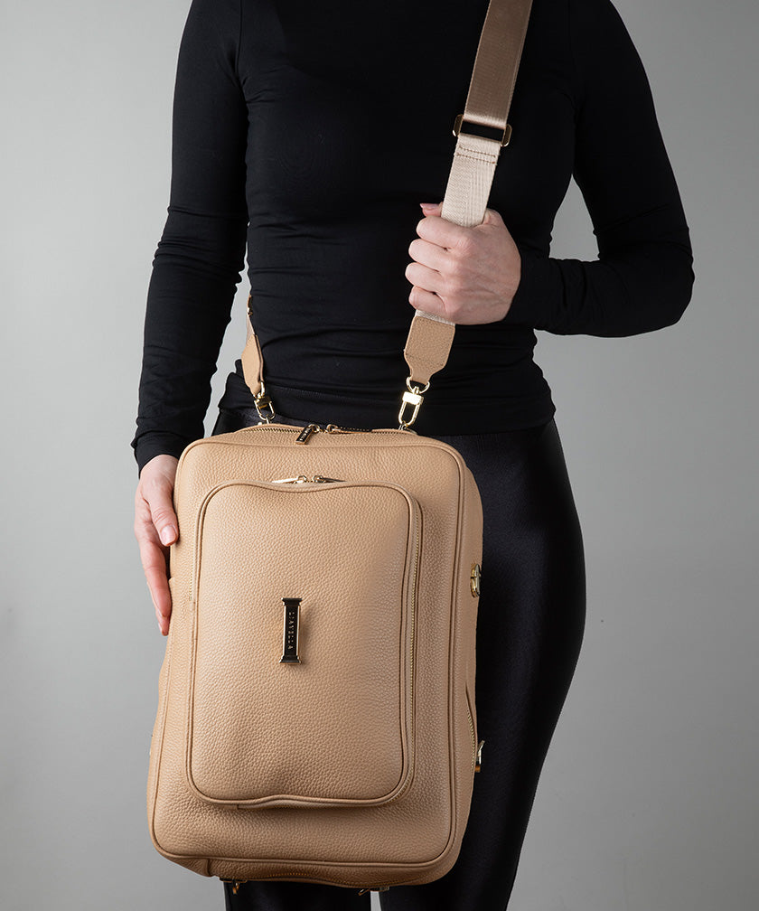 Person holding a crème caramel AVAIA crossbody bag against a gray background