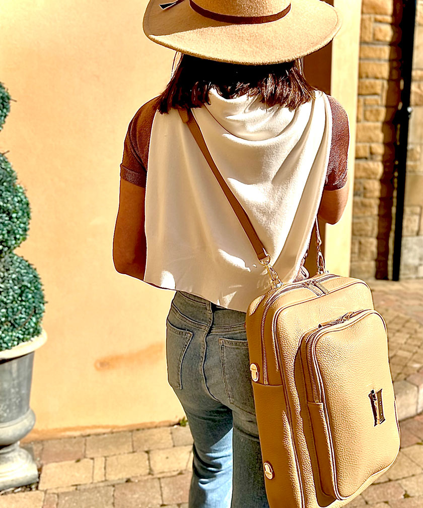 Person wearing a beige hat and carrying a crème caramel AVAIA crossbody bag backpack on a sunny day.