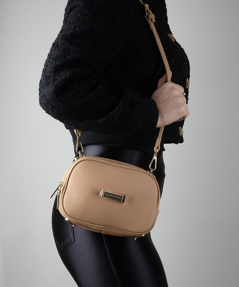 Person wearing a crème caramel AVAIA Petit bag as a shoulder bag against a gray background.