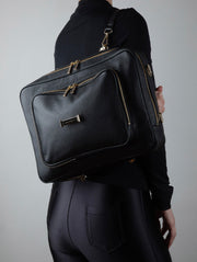 Person wearing an AVAIA bag in noir as a backpack with gold zippers on a plain background