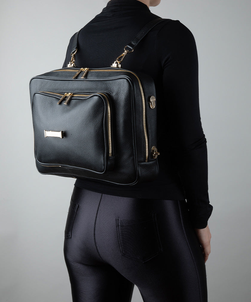 Person wearing a black AVAIA bag as a backpack with gold zippers on a gray background