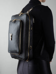 Person wearing a black leather AVAIA bag as a backpack with gold zippers on a gray background