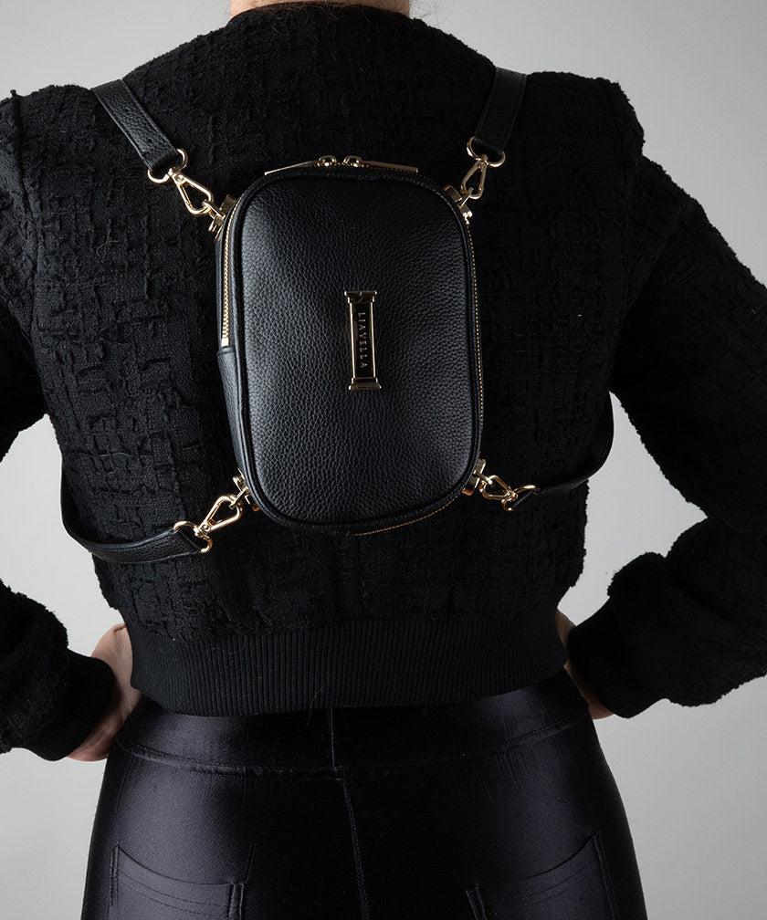 Person wearing a black textured sweater with a the AVAIA Petit in noir worn as a baby backpack featuring a gold brand logo.