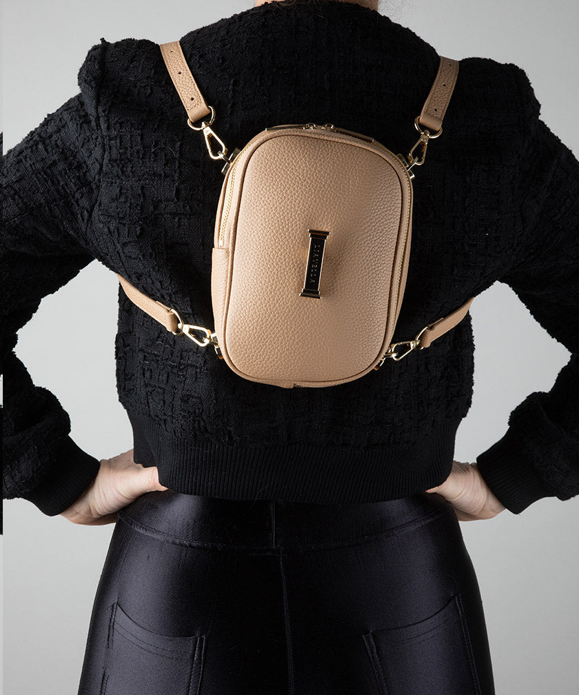 Person wearing a AVAIA Petit in crème caramel with two leather straps as a backpack with a black sweater and pants on a light gray background