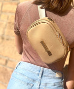 Load image into Gallery viewer, Person wearing a crème caramel AVAIA Petit as a crossbody bag with a blurred background