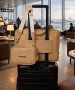 Load image into Gallery viewer, The leather bags AVAIA crème caramel on suitcase using pass-through strap and the AVAIA Petit crème caramel held by suitcase handles, in an airport lounge.