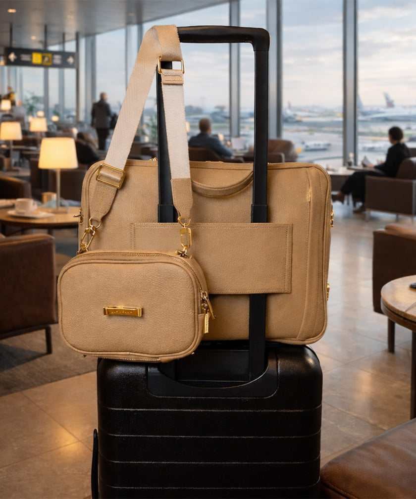 The leather bags AVAIA crème caramel on suitcase using pass-through strap and the AVAIA Petit crème caramel held by suitcase handles, in an airport lounge.
